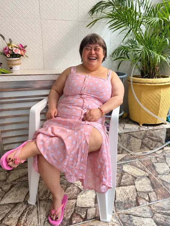 Maria Isabel, a Betinha, sorrindo sentada em um quintal